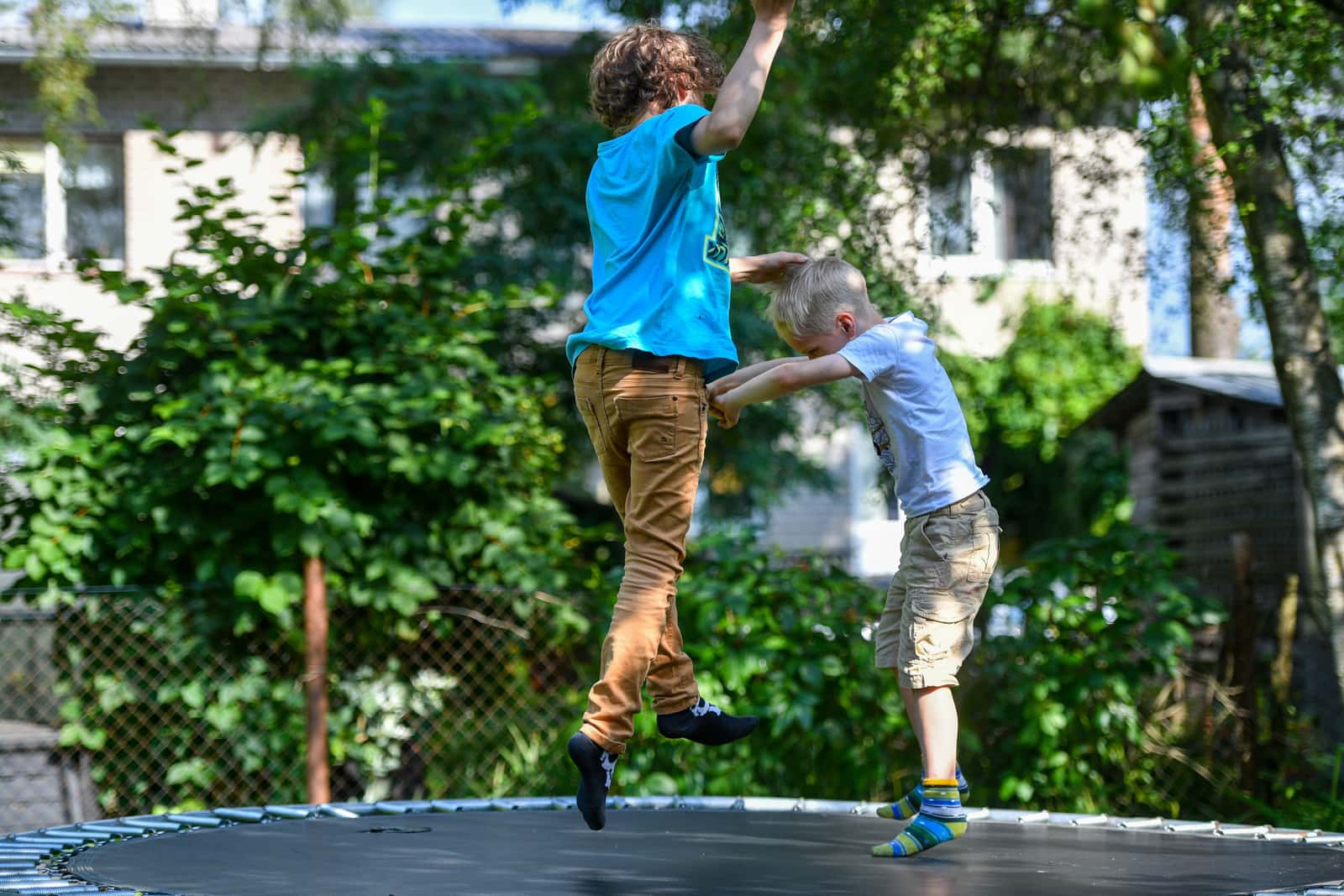 Two kids on a backyard trampoline on a sunny day