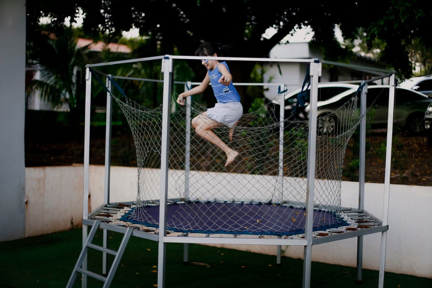 Young girl jumping on a backyard trampoline inside its enclosure net