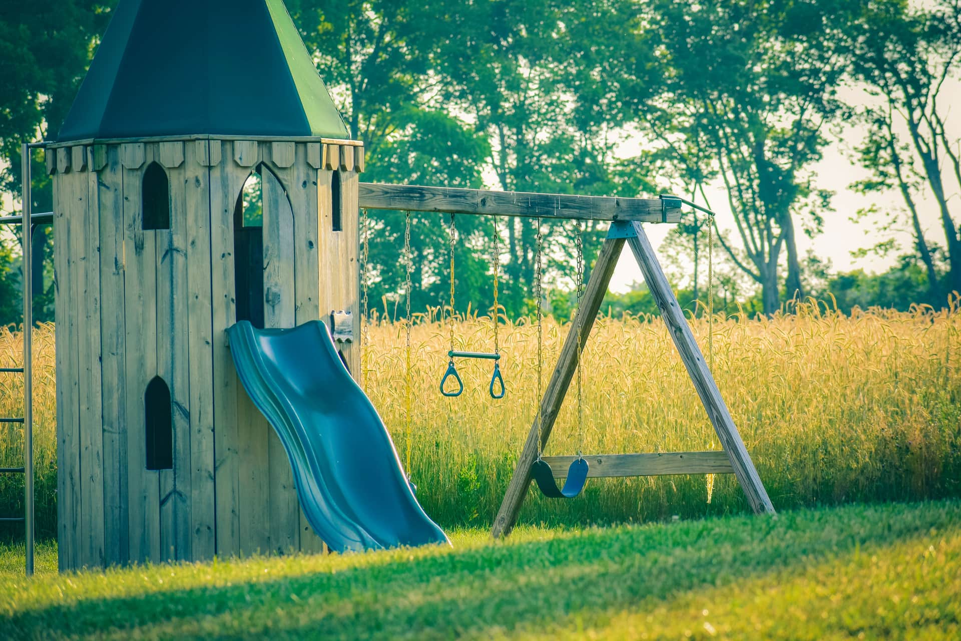 Wooden tower playset with a slide beside a green meadow