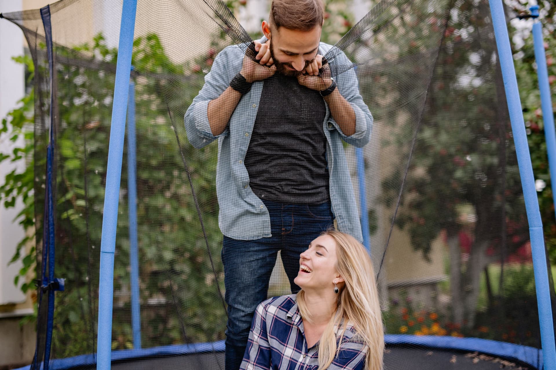Couple standing behind the enclosure net of a backyard trampoline